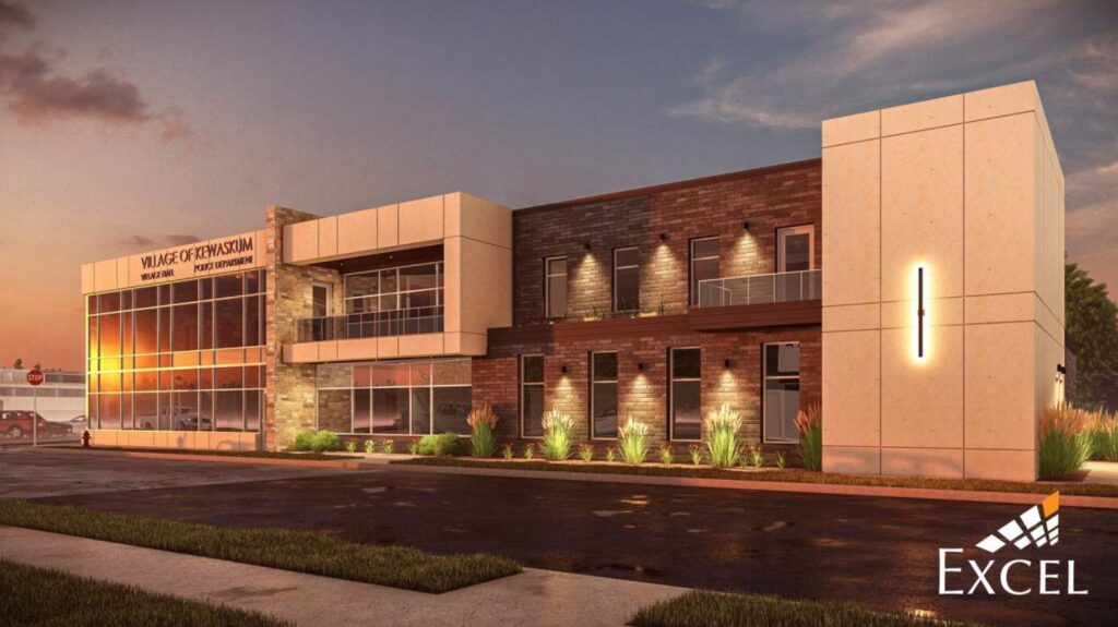 Architectural rendering of the proposed new Village of Kewaskum building. The modern, two-story brick and stone structure features large windows on both floors. Landscaping includes grass and small shrubs. The building is shown at dusk, with interior and exterior lighting illuminating the space. The "Village of Kewaskum" signage is prominently displayed on the front facade.