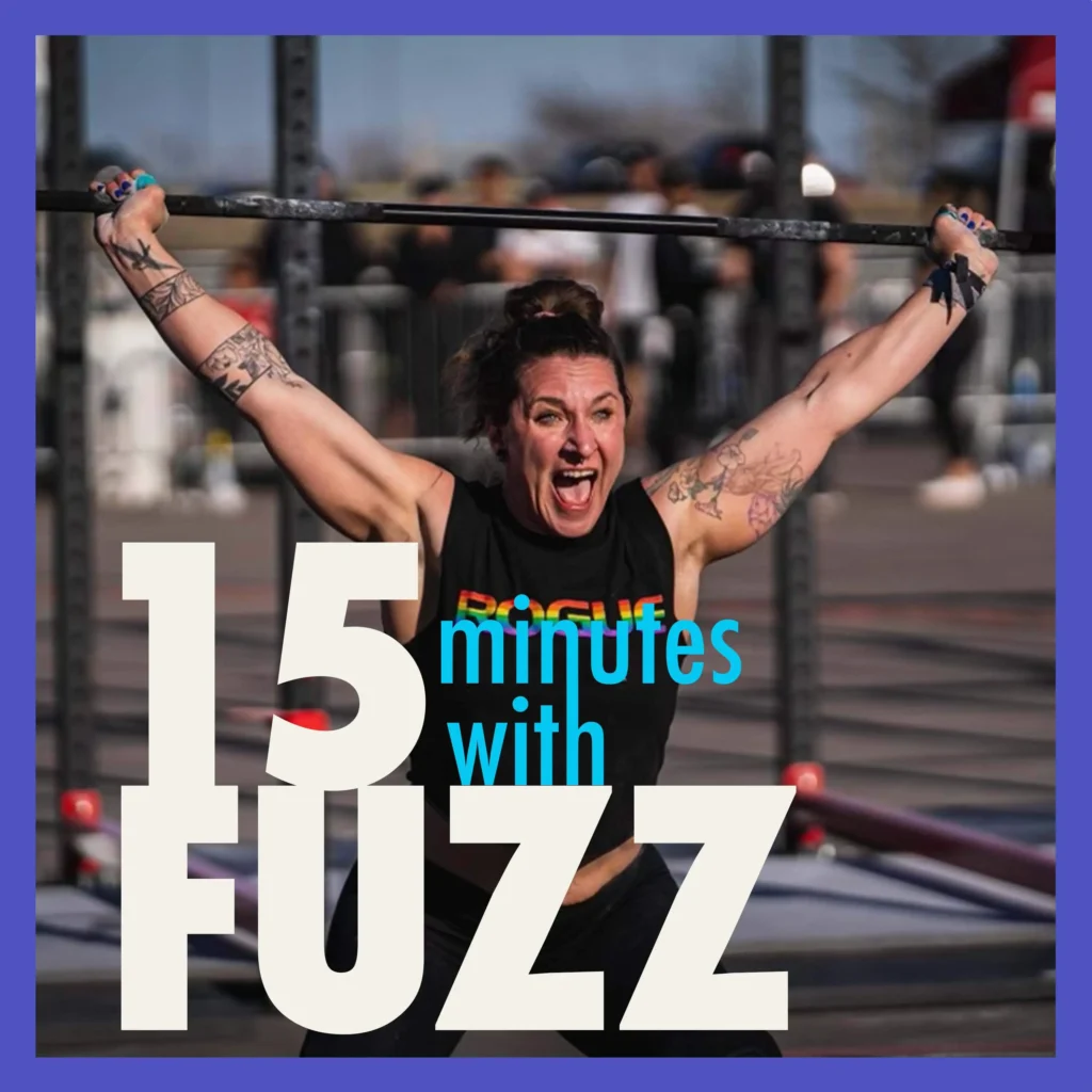 A woman is lifting a barbell overhead during a fitness competition. She is wearing a black tank top with the word “Rogue” in rainbow letters and has multiple tattoos on her arms. Her expression is one of intense effort and determination. The background is blurred, showing other competitors and equipment. The image is framed with a purple border and has the text “15 minutes with FUZZ” in large white and blue letters overlaying the bottom portion of the photo.