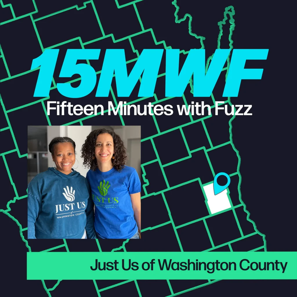 A vibrant graphic featuring the text “15MWF” in bold, bright turquoise letters at the top. Below it, the full name “Fifteen Minutes with Fuzz” is written in white. The background includes a map outline in green, with a highlighted area pinpointed in white and blue, indicating a specific location. At the bottom, there is a rectangular photo of two women, both smiling, wearing shirts with the “Just Us” logo. Below the photo, the text “Just Us of Washington County” is displayed in green on a black strip.