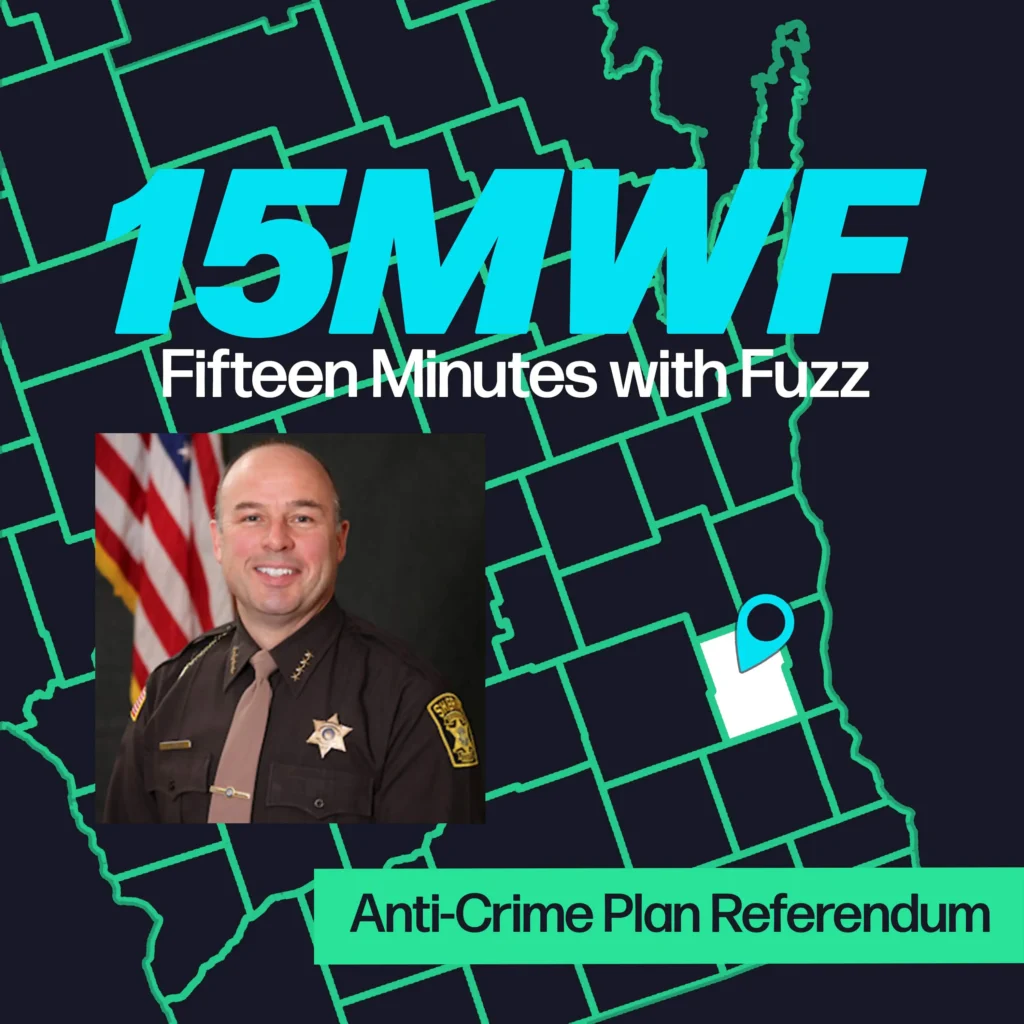 A graphic for “Fifteen Minutes with Fuzz” features a background map outline in green on a dark blue background. The title “15MWF” in large teal letters is at the top, with “Fifteen Minutes with Fuzz” in white letters underneath. Below the title, there is an inset photo of a sheriff in uniform, smiling, with the American flag in the background. At the bottom, a green label reads “Anti-Crime Plan Referendum.”
