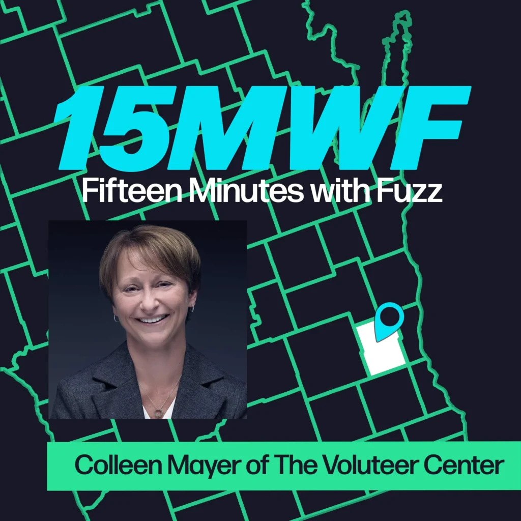 A graphic for “Fifteen Minutes with Fuzz” features a background map outline in green on a dark blue background. The title “15MWF” in large teal letters is at the top, with “Fifteen Minutes with Fuzz” in white letters underneath. Below the title, there is an inset photo of a woman with short brown hair, wearing a dark blazer and smiling at the camera against a dark background. At the bottom, a green label reads “Colleen Mayer of The Volunteer Center.”