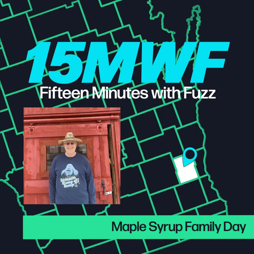 A graphic for “Fifteen Minutes with Fuzz” features a background map outline in green on a dark blue background. The title “15MWF” in large teal letters is at the top, with “Fifteen Minutes with Fuzz” in white letters underneath. Below the title, there is an inset photo of a man wearing a blue sweatshirt with a graphic of a gorilla and text, standing in front of a red wooden structure. He is also wearing a hat. At the bottom, a green label reads “Maple Syrup Family Day.”