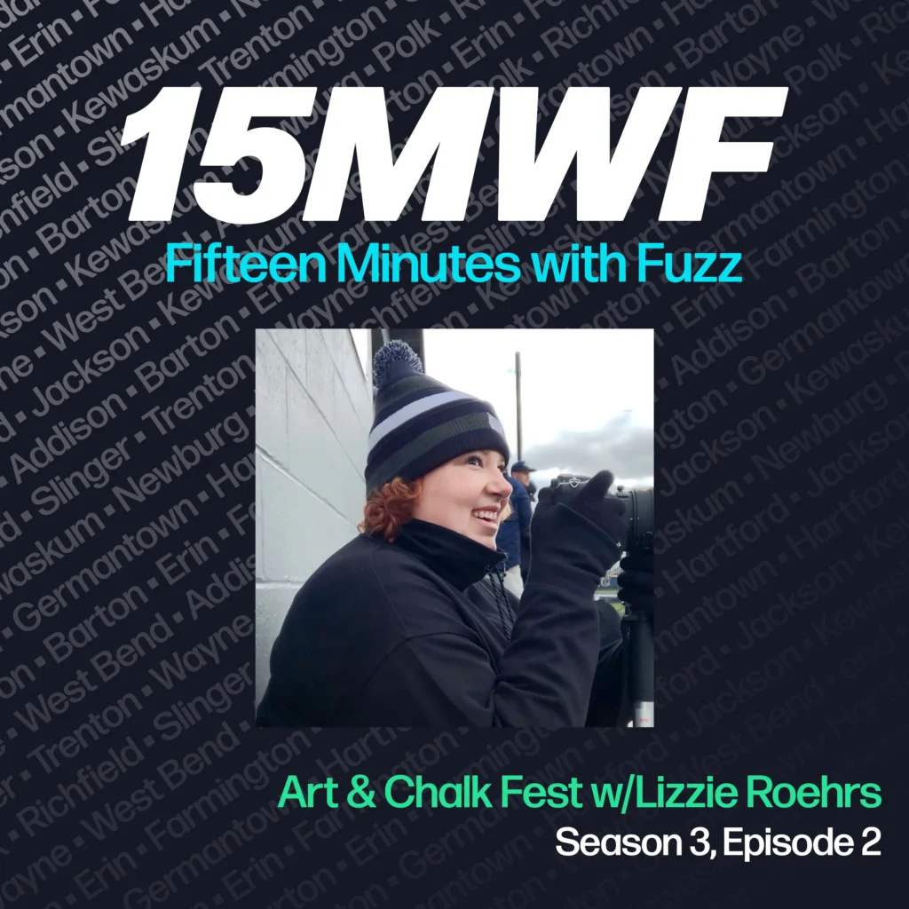 The cover art features a photo of Lizzie Roehrs, warmly dressed and smiling, possibly in the midst of capturing the event on camera. The podcast title “15MWF - Fifteen Minutes with Fuzz” is prominently displayed at the top. The background includes a pattern of names of different locations within Washington County, emphasizing the local focus of the podcast. The episode title “Art & Chalk Fest w/Lizzie Roehrs” is written at the bottom, along with the season and episode number.
