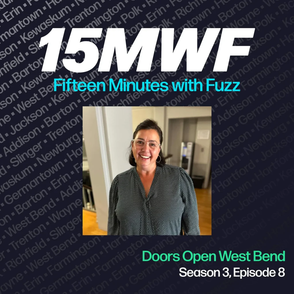 The cover art features a smiling woman in a black and white patterned blouse, representing her involvement with the Doors Open West Bend event. The podcast title “15MWF - Fifteen Minutes with Fuzz” is prominently displayed at the top. The background includes a pattern of names of different locations within Washington County, emphasizing the local focus of the podcast. The episode title “Doors Open West Bend” is written at the bottom, along with the season and episode number.