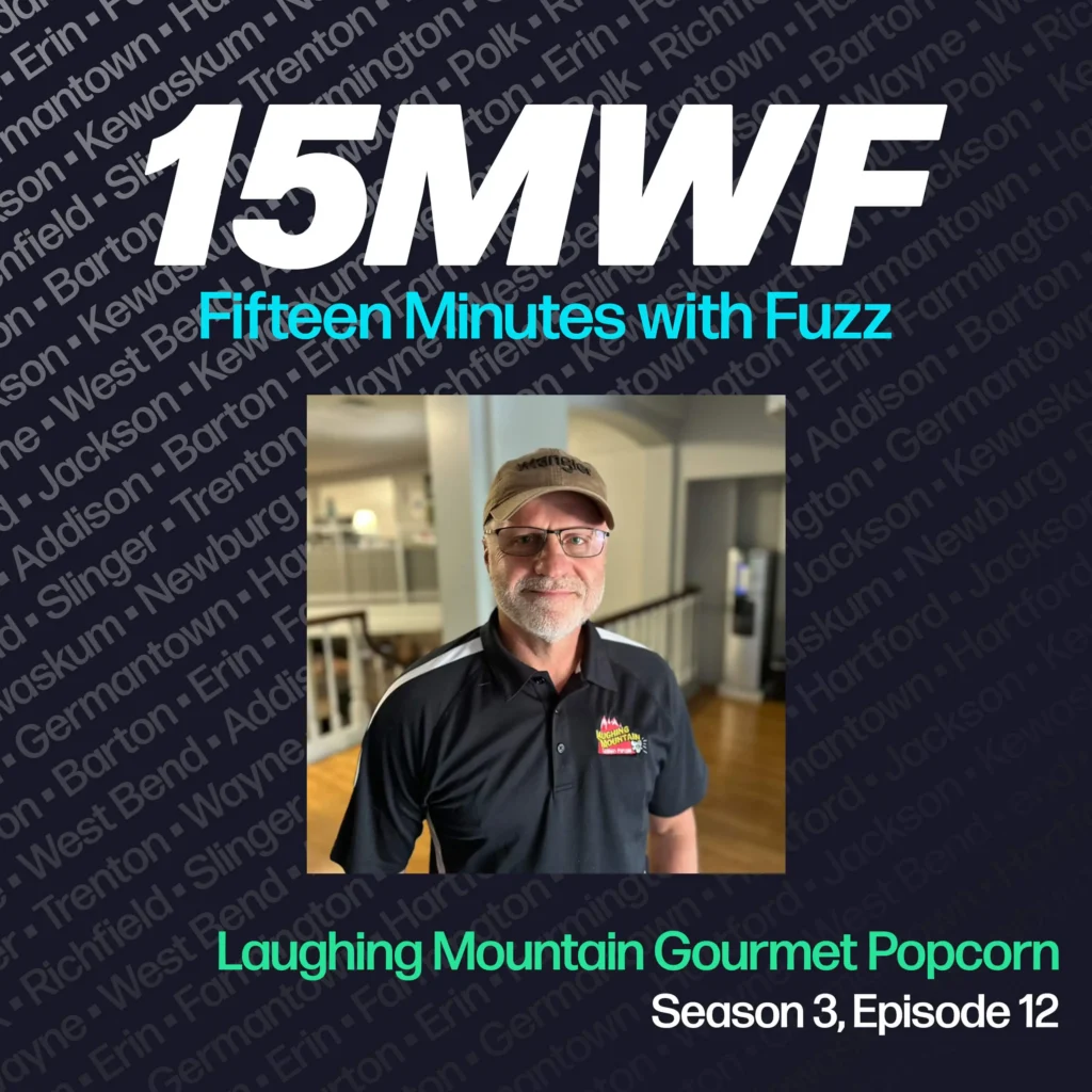 15MWF - Fifteen Minutes with Fuzz podcast cover art for Season 3, Episode 12 featuring a representative from Laughing Mountain Gourmet Popcorn. The background includes names of various locations within Washington County, emphasizing the local focus of the podcast. The guest is standing and smiling, wearing a cap and a company-branded shirt.