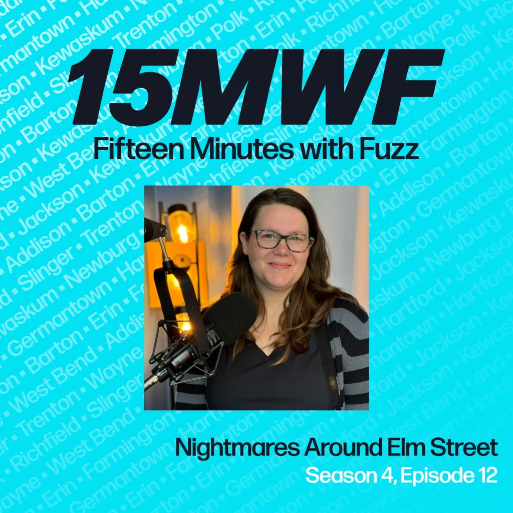 A square promotional graphic for the “Fifteen Minutes with Fuzz” podcast, featuring the title “Nightmares Around Elm St.” and “Season 4, Episode 12” beneath a photo of Emily Greene. She is seen in a recording studio, wearing glasses, smiling, and speaking into a microphone. The background is light blue with faint town names, and the podcast’s title “15MWF: Fifteen Minutes with Fuzz” is prominently displayed at the top.