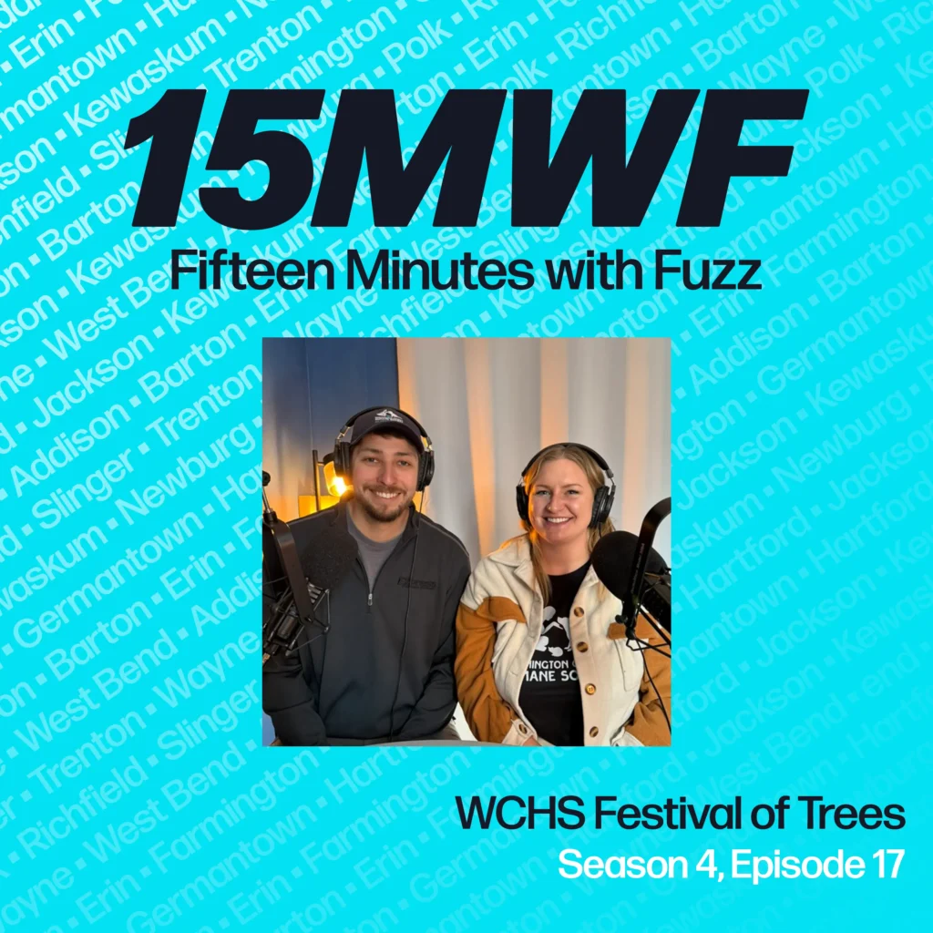 A promotional graphic for the podcast “Fifteen Minutes with Fuzz” featuring the hosts of the Washington County Humane Society Festival of Trees episode. The background is light blue with text listing community names such as West Bend, Kewaskum, and Germantown in a subtle pattern. The logo “15MWF” is prominently displayed at the top, with the text “Fifteen Minutes with Fuzz” underneath. Below, a photo of two smiling people wearing headphones is shown, sitting in a recording studio. The episode title reads: “WCHS Festival of Trees, Season 4, Episode 17.
